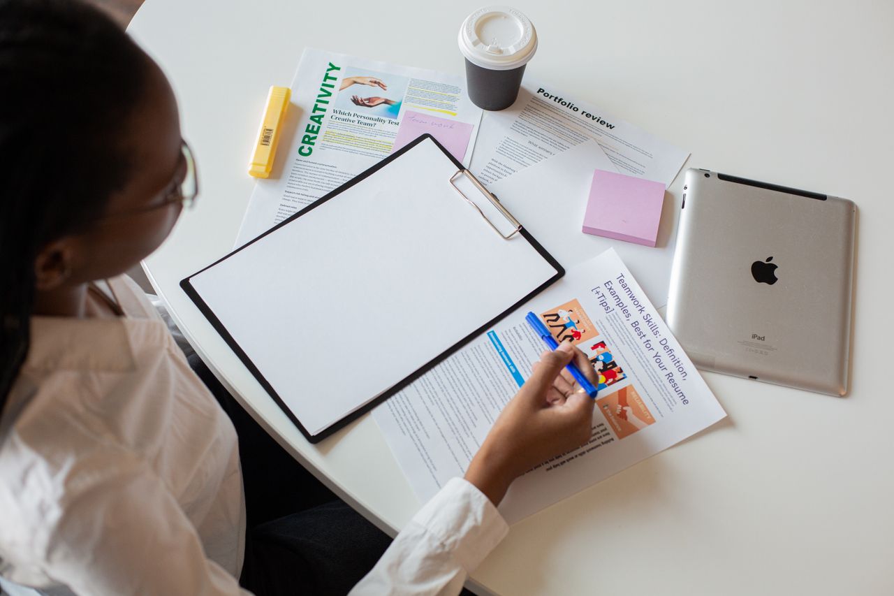 Vue de dessus d’une femme examinant différents documents avec un clipboard sur un bureau.